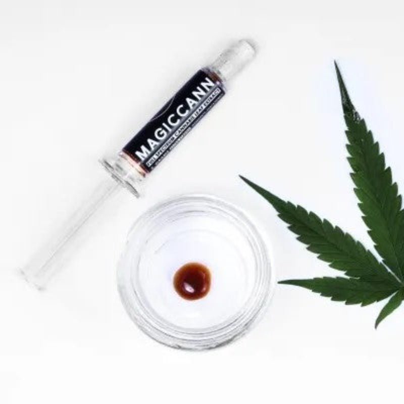 Glass syringe with "MAGICANN" label, glass dish with medical cannabis oil, and cannabis leaf.