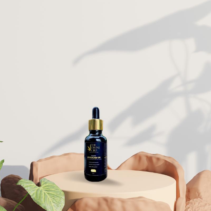 Bottle of Paarmi Cares "The Divine CBD" ANXOCBDAM OIL on a beige pedestal with surrounding rocks and a plant in the background.