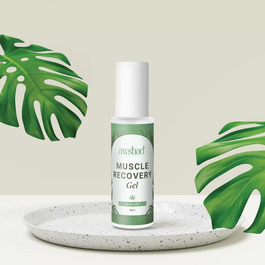 A bottle of awshad cbd muscle recovery gel on a speckled plate with tropical leaves in the background.
