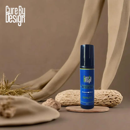 Blue bottle labelled 'Cure By Design Anxiety therapeutic body oil' on a textured surface with natural elements.