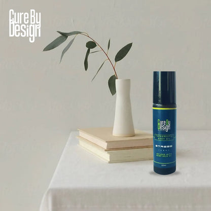 Bottle of Cure By Design Therapeutic Body Oil for Stress, on a table with a vase and books in the background
