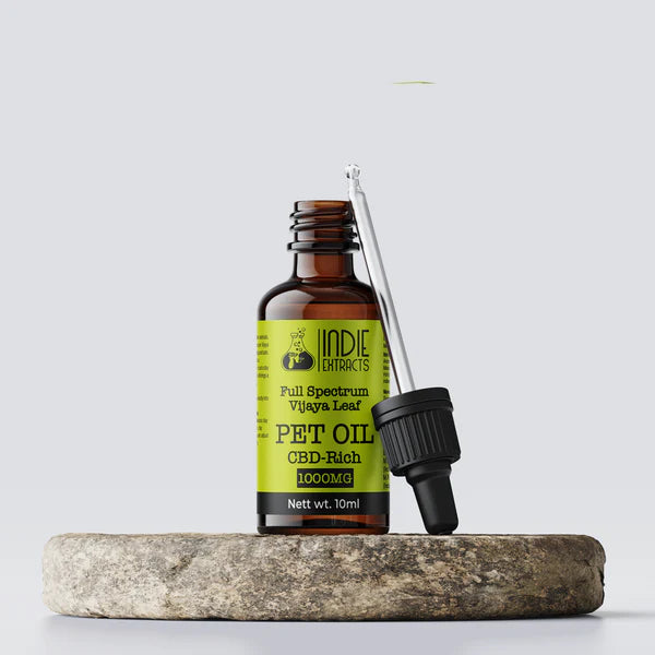 Bottle of Indie Extracts Pet Oil with dropper on a stone surface against a light gray background.