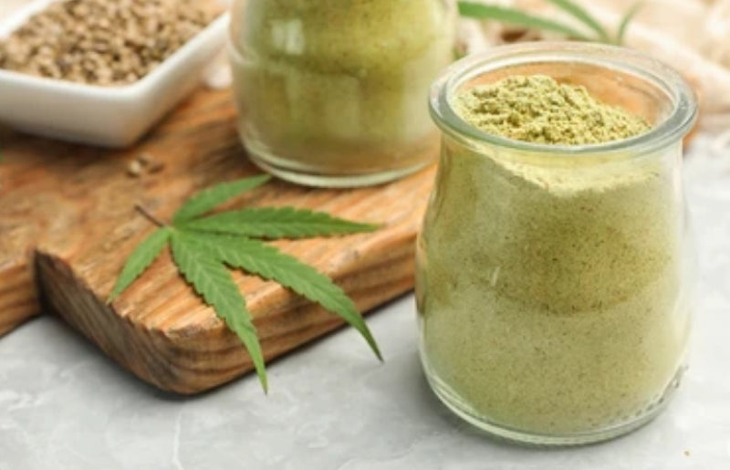 Two glass jars with green powder on a wooden board with a cannabis leaf.