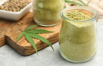 Two glass jars with green powder on a wooden board with a cannabis leaf.