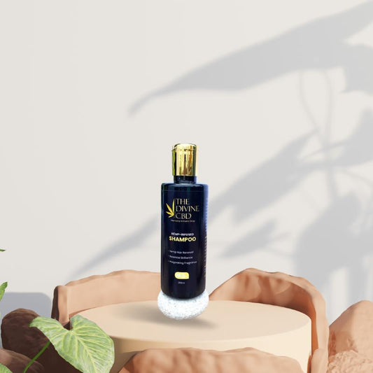 Bottle of "The Divine CBD" hemp-infused shampoo on a rounded platform with plant shadows in the background.

