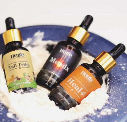 Three CBD oil bottles from hebe wellness on a blue plate with white powder.

